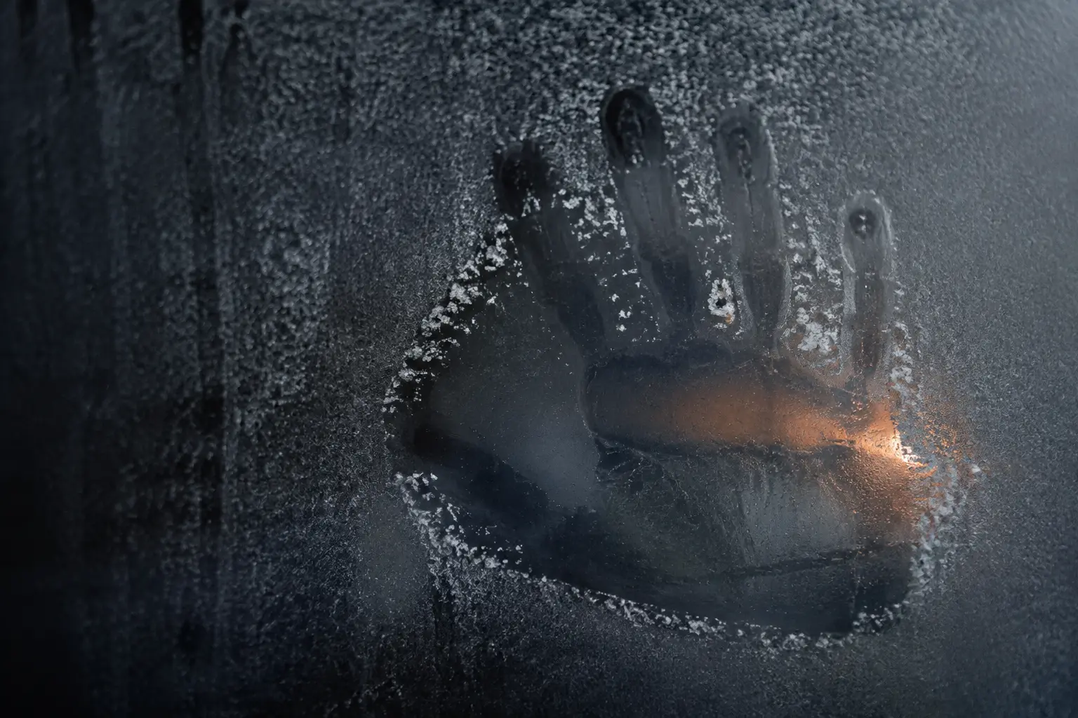 A handprint clearing a precise window through frost on dark glass